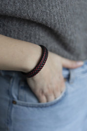 Geflochtenes schwarz-rotes Armband am Handgelenk, blaue Hose, grauer Pulli